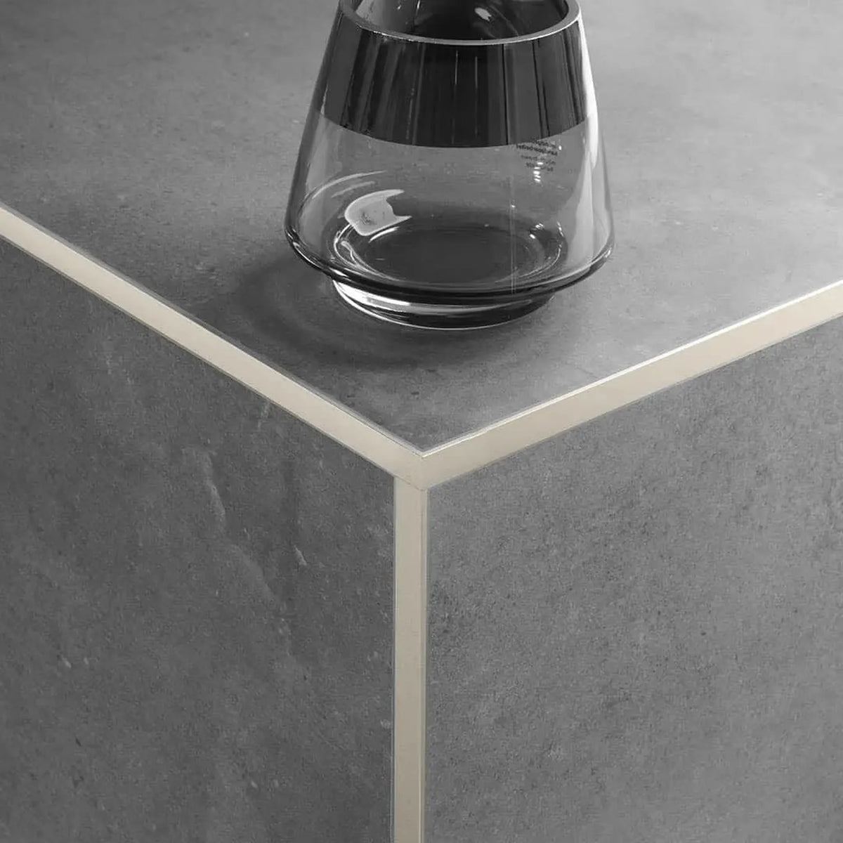 Sand-coloured powder-coated angle profile made of aluminium with narrow visible edge and matt appearance, installed on the outside corner under dark tile covering.