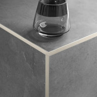 Sand-coloured powder-coated angle profile made of aluminium with narrow visible edge and matt appearance, installed on the outside corner under dark tile covering.
