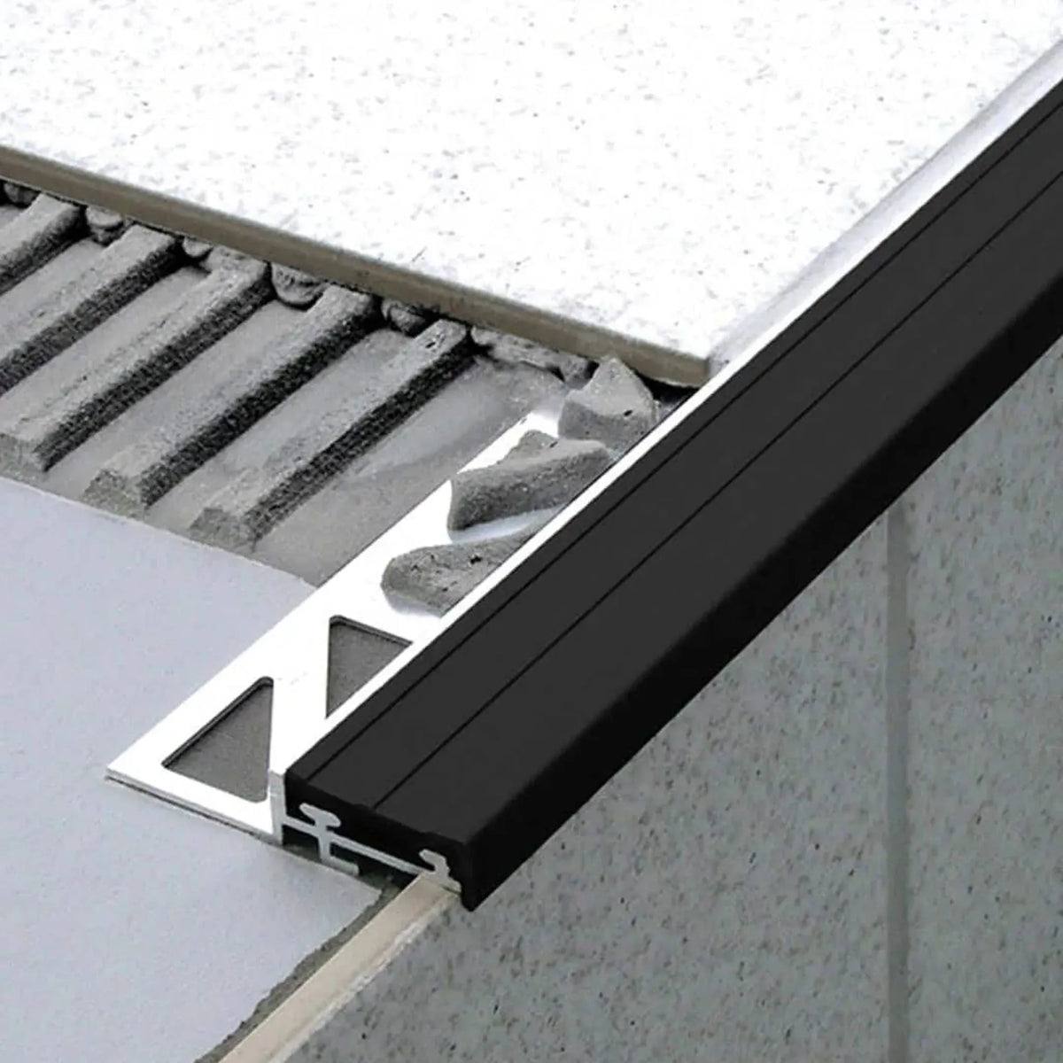 Unter Fliese verbautes Treppenprofil mit schmaler Gummieinlage in Schwarz. Ein Teil des gestanzten Schenkels liegt frei im Kleberbett #A0001744 #A0001748